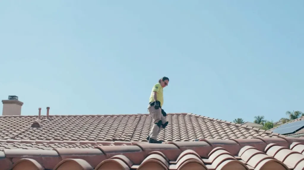A roof inspector carefully walks along a Spanish tile roof under a clear blue sky during a home inspection in Miami.